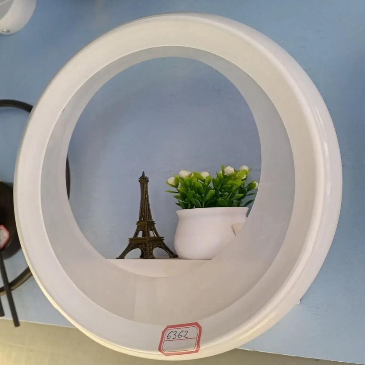 A circular, white wall shelf, shaped like a hollow ring